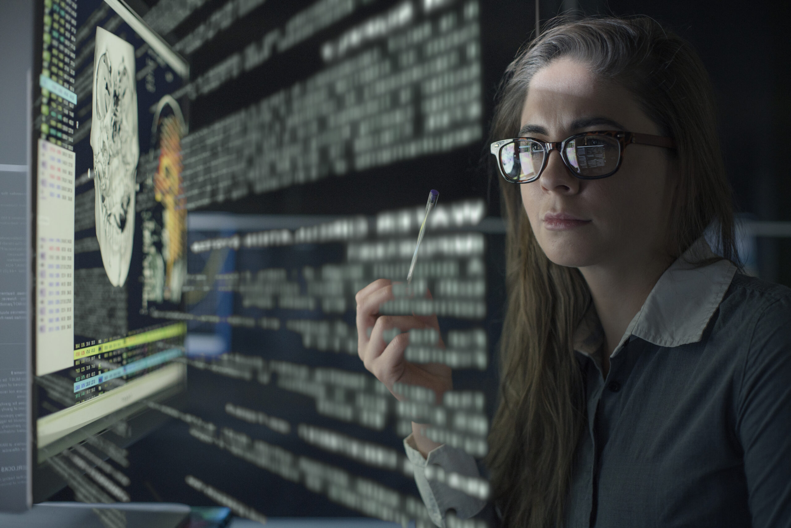 Stock photo of a pretty young woman looking at a computer monitor displaying aspects of human physiology and a see through text display.