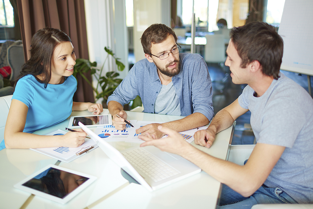 Group of three successful business partners in casual discussing ideas at meeting in office