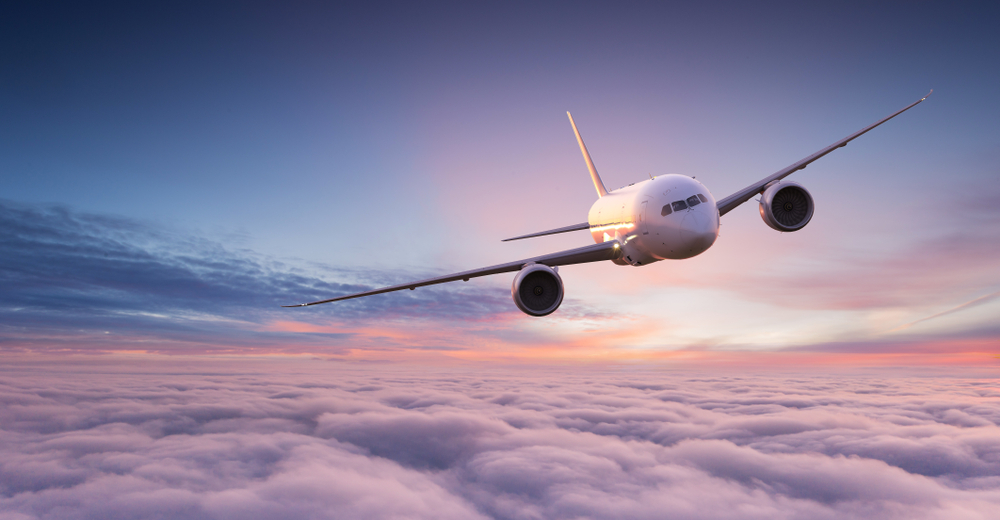 commercial airplane jetliner flying above dramatic clouds in beautiful sunset pink and blue light sky